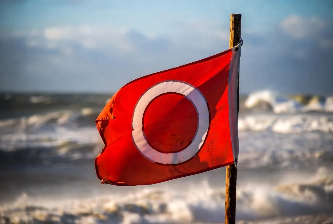 Red warning flag flying at the edge of a heavy Pacific surf beach